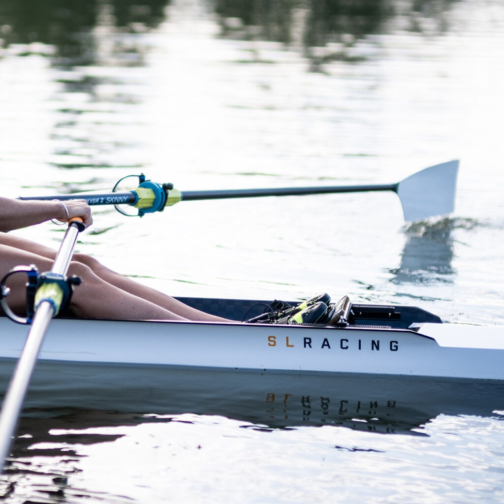 Close up of an SL Racing single scull on the Clive River. You can see the logo on the boat and two oars int water.